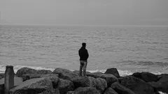 Hombre en chaqueta negra de pie sobre roca junto al mar