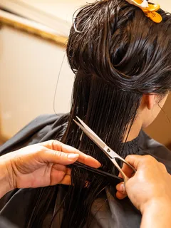 Mujer joven cortando cabello de otra en peluquería con tijeras