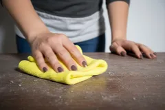Persona limpiando mesa de madera con paño amarillo, higiene y orden en el hogar