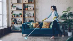 Mujer feliz limpiando y bailando con auriculares inalámbricos en apartamento loft