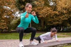 Mujeres haciendo ejercicio al aire libre, sentadillas y flexiones en parque otoñal.