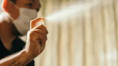Hombre con mascarilla médica aplicando desinfectante para evitar coronavirus en casa